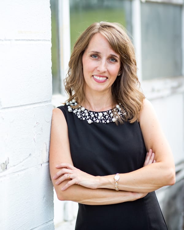 Teresa Huff headshot, arms crossed, white brick